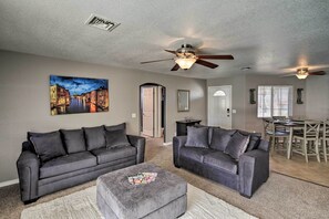 A living room with two grey sofas, a coffee table, a ceiling fan, and a dining area with a table and chairs. - Lake Havasu City Retreat w/ Patio & Grill (Lake Havasu City)