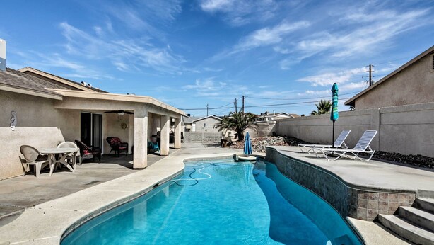 A swimming pool with a curved design, surrounded by a patio area with chairs and a table. - Lake Havasu City Retreat w/ Patio & Grill (Lake Havasu City)