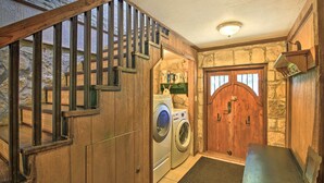 A laundry room with a wooden staircase, a washing machine, a dryer, and a rustic stone wall. - Countryside Cottage: 17 Mi to Downtown San Antonio (San Antonio)