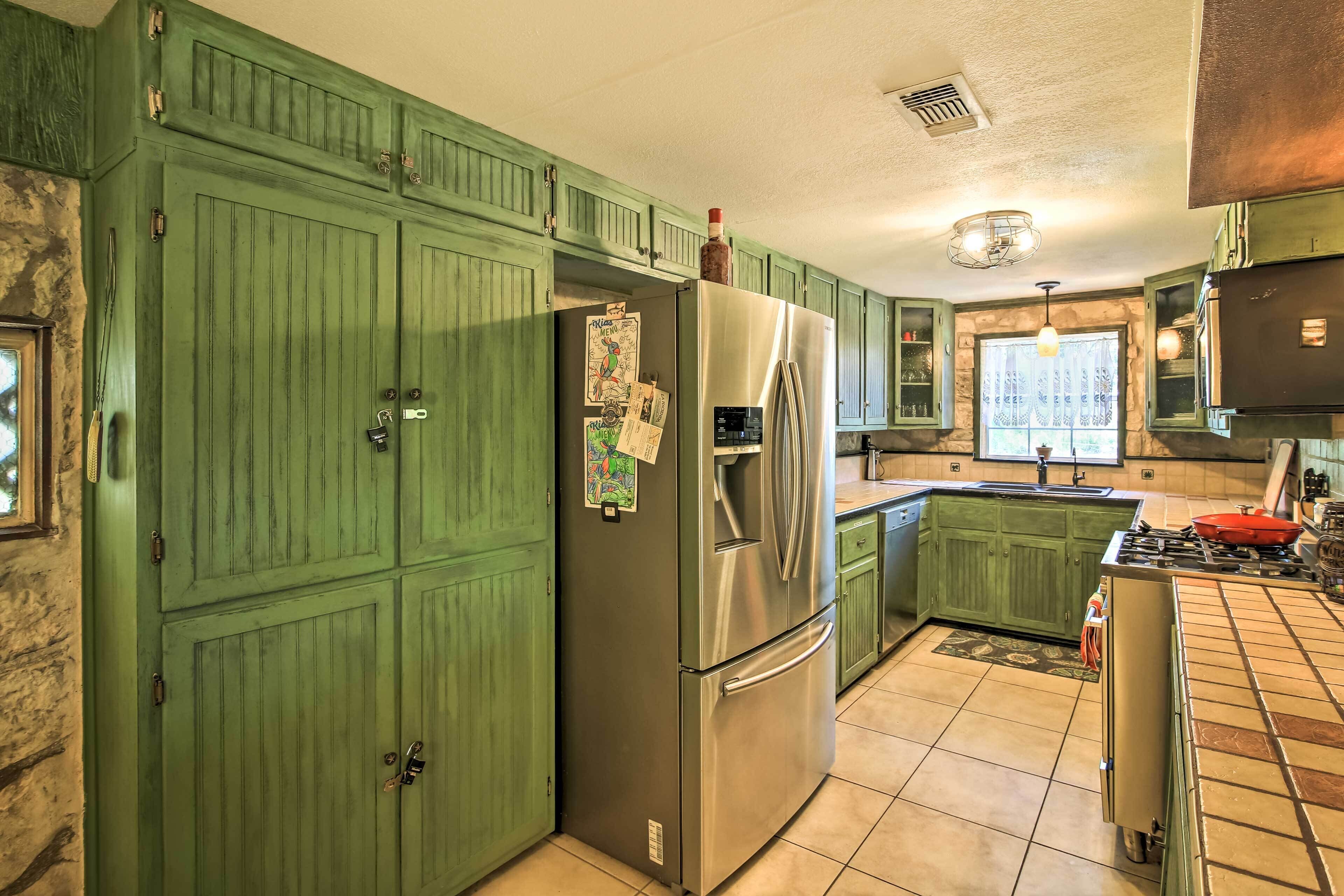 A kitchen with green cabinets, a stainless steel refrigerator, a gas stove, and a window with a view.