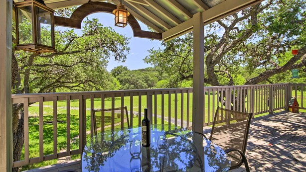 A glass table with two empty glasses and a bottle, under a wooden pergola with hanging lanterns, overlooking a grassy area with trees. - Countryside Cottage: 17 Mi to Downtown San Antonio (San Antonio)
