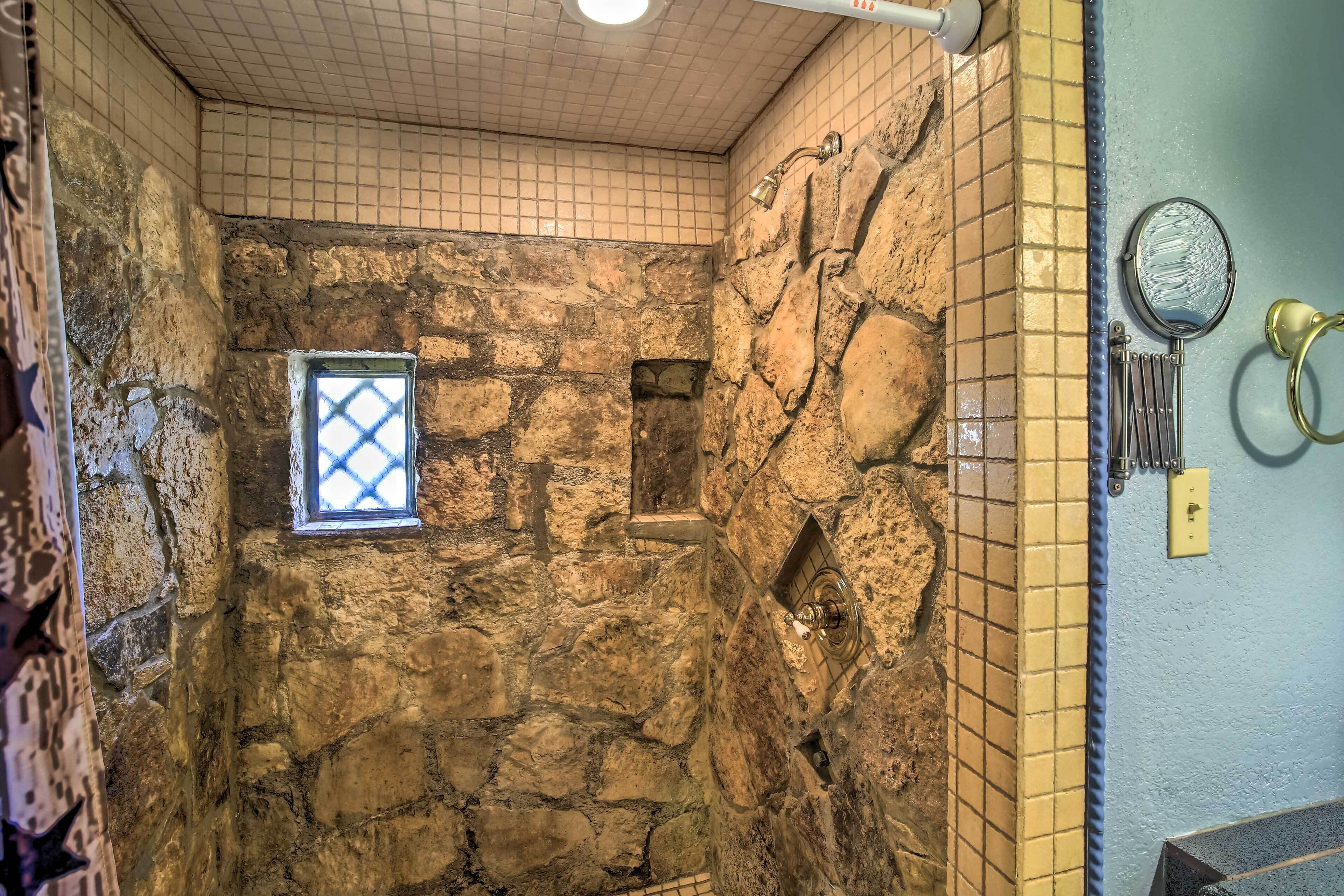 Un baño con paredes de piedra, una ventana pequeña, un perchero y un espejo.