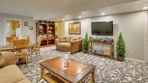 A living room with a sofa, chairs, a coffee table, a bookshelf, a TV, and decorative plants. - Farr West Apartment on Farm < 25 Mi to Ski Resorts (Ogden)