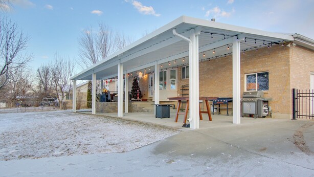 A covered patio area with a brick building, a Christmas tree, and outdoor cooking equipment. - Farr West Apartment on Farm < 25 Mi to Ski Resorts (Ogden)