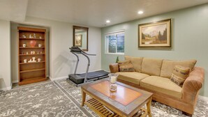 A living room with a treadmill, a sofa, a coffee table, and a bookshelf. - Farr West Apartment on Farm < 25 Mi to Ski Resorts (Ogden)