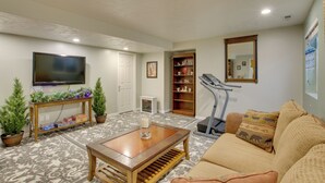 A living room with a television, a treadmill, a sofa, a coffee table, and a bookshelf. - Farr West Apartment on Farm < 25 Mi to Ski Resorts (Ogden)