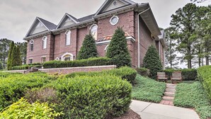 A large brick building with a symmetrical facade, multiple windows, and a well-maintained garden with hedges and a pathway leading to a seating area. - Anderson Creek Club Condo w/ Community Amenities! (Spring Lake)