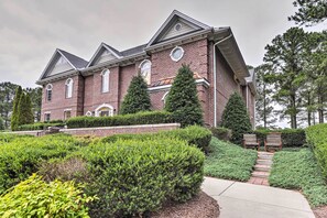 A large brick building with a symmetrical facade, multiple windows, and a well-maintained garden with hedges and a pathway leading to a seating area.