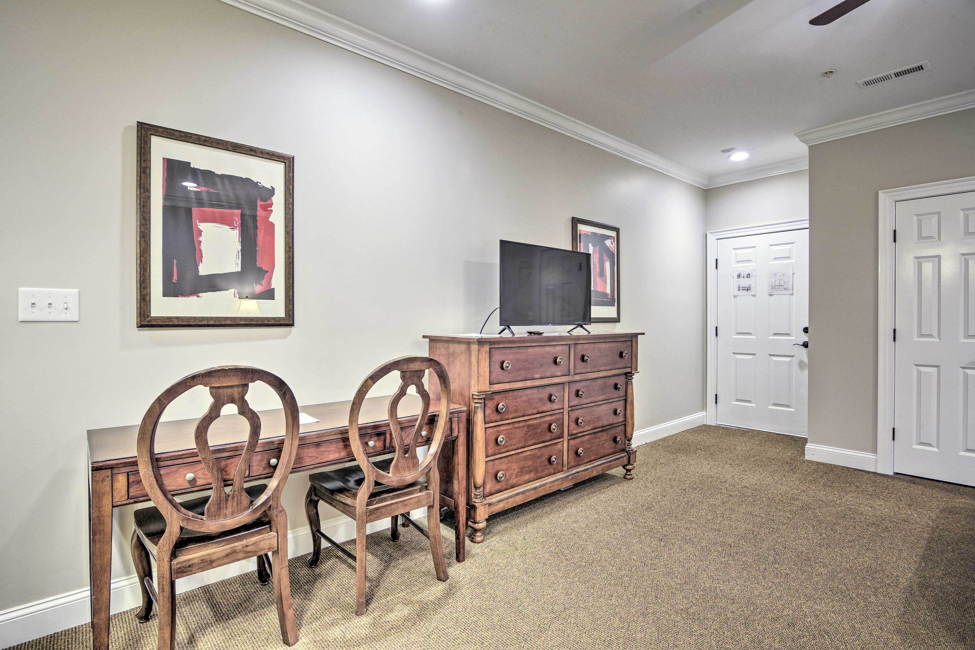 A room with a desk, two chairs, a dresser, and a television.