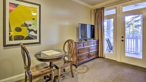 A room with a round table, a wooden chair, a dresser with a television, and a door leading to an outdoor area with a view of trees. - Anderson Creek Club Condo w/ Community Amenities! (Spring Lake)
