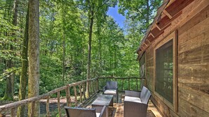 Eine Holzterrasse mit Korbmöbeln und einem Glasgeländer mit Blick auf einen Wald.