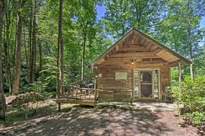 Une cabane en bois dotée d’un porche et d’une petite terrasse, entourée d’une forêt.