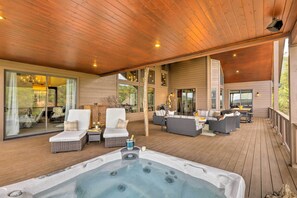 Une vaste terrasse extérieure dotée d’un jacuzzi, de coins salon et de grandes fenêtres offrant une vue sur le paysage environnant.
