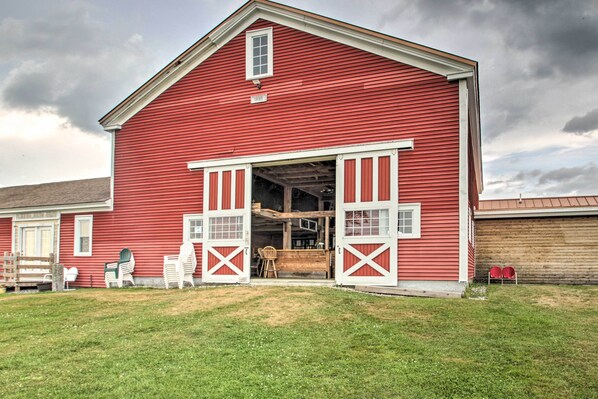 A red barn with open doors, a wooden bench, and two Adirondack chairs outside.