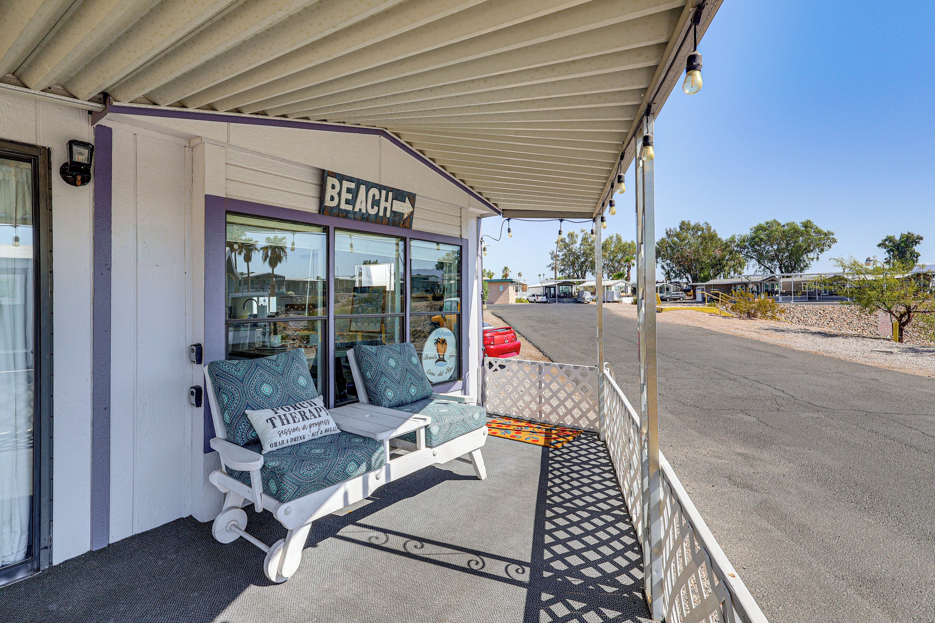 A beach-themed establishment with a covered porch, outdoor seating with patterned cushions, and a sign indicating the direction to the beach.