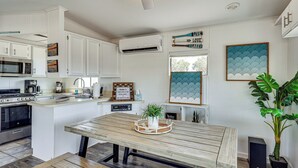 Una cocina moderna con armarios blancos, microondas integrado y estufa. Hay una mesa de comedor de madera con una bandeja y una planta en maceta.