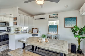 Una cocina moderna con armarios blancos, microondas integrado y estufa. Hay una mesa de comedor de madera con una bandeja y una planta en maceta.