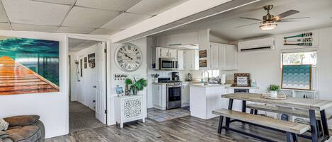 A spacious kitchen with white cabinetry, a wooden dining table, and a large clock on the wall.