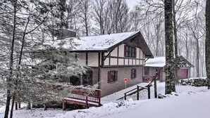 A traditional timber-framed house with a steeply pitched roof, surrounded by snow-covered trees and a wooden staircase leading to the entrance.