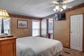 A bedroom with a bed, a ceiling fan, a TV mounted on the wall, and a door. - Ooltewah Cabin w/ Grill, Pool Table & Porch! (Ooltewah)