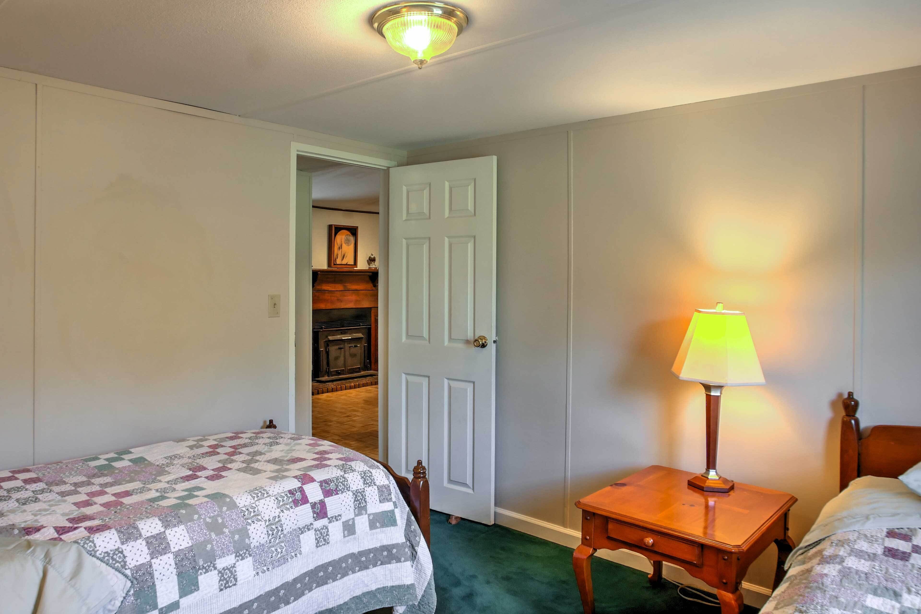 Une chambre avec deux lits, une table de chevet avec une lampe, une porte donnant sur un couloir et une cheminée au fond de la pièce.