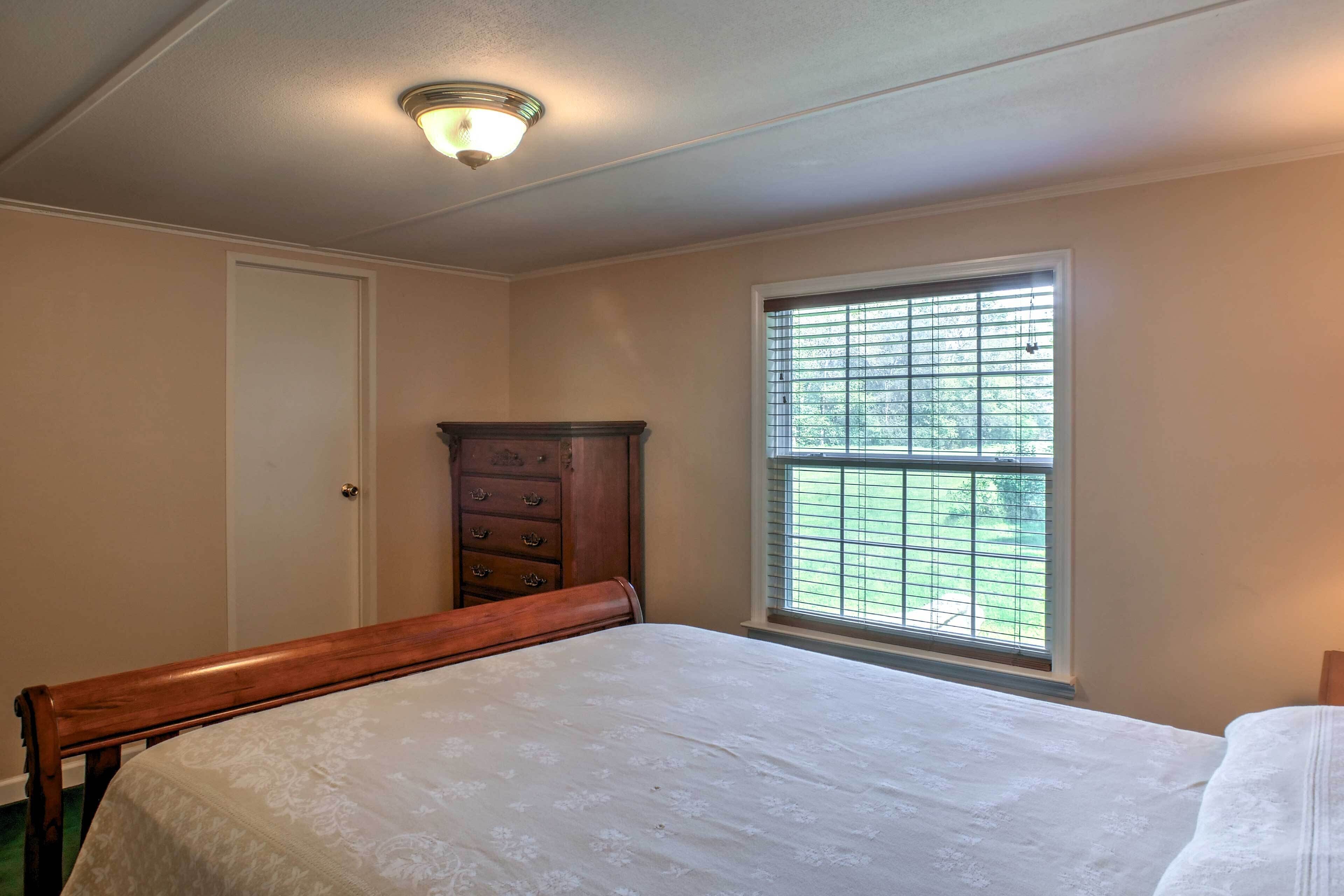 A bedroom with a bed, a dresser, and a window with blinds.