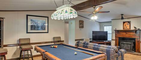 A pool table in a living room with a ceiling fan, a fireplace, and a television.