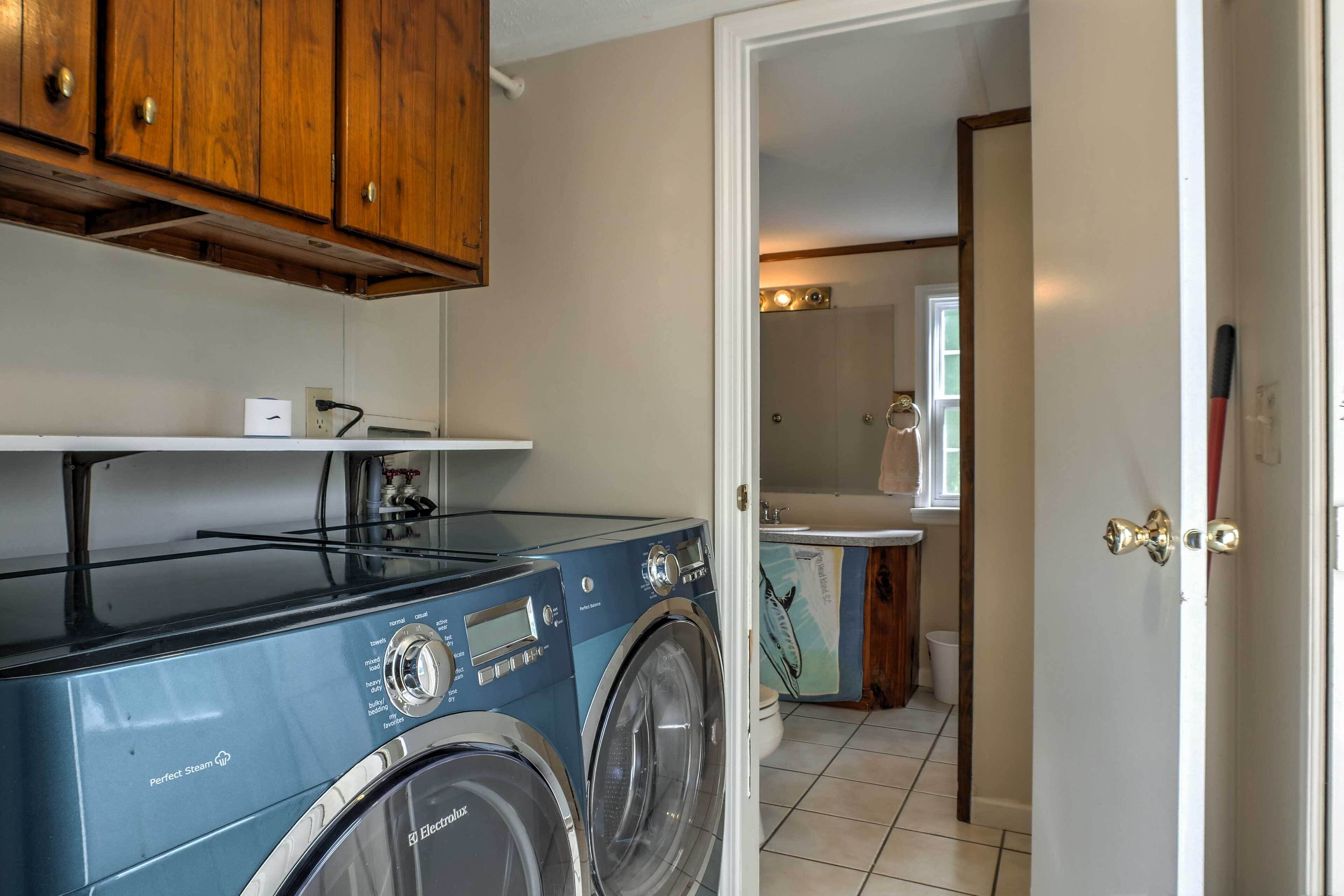 A laundry area with a washing machine and dryer, wooden cabinets, and a bathroom visible through an open door.