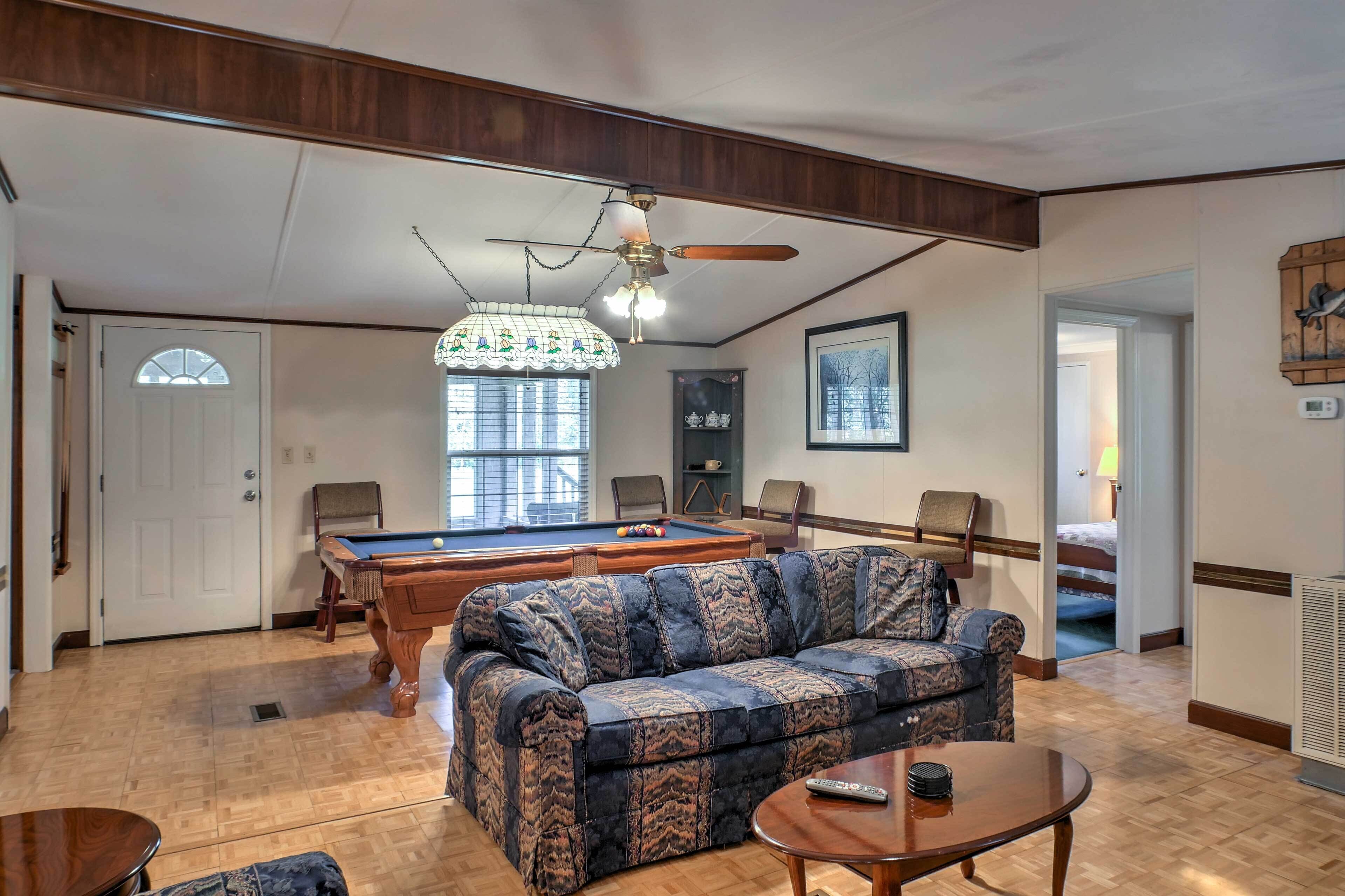 A room with a pool table, a sofa, a ceiling fan, and a chandelier.