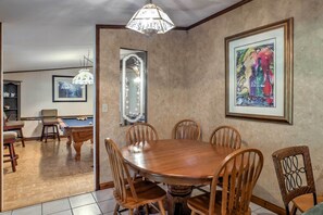 A dining area with a wooden table and chairs, a pool table, and a chandelier. - Ooltewah Cabin w/ Grill, Pool Table & Porch! (Ooltewah)