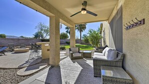 An outdoor patio area with wicker furniture, a ceiling fan, and a view of a landscaped garden.