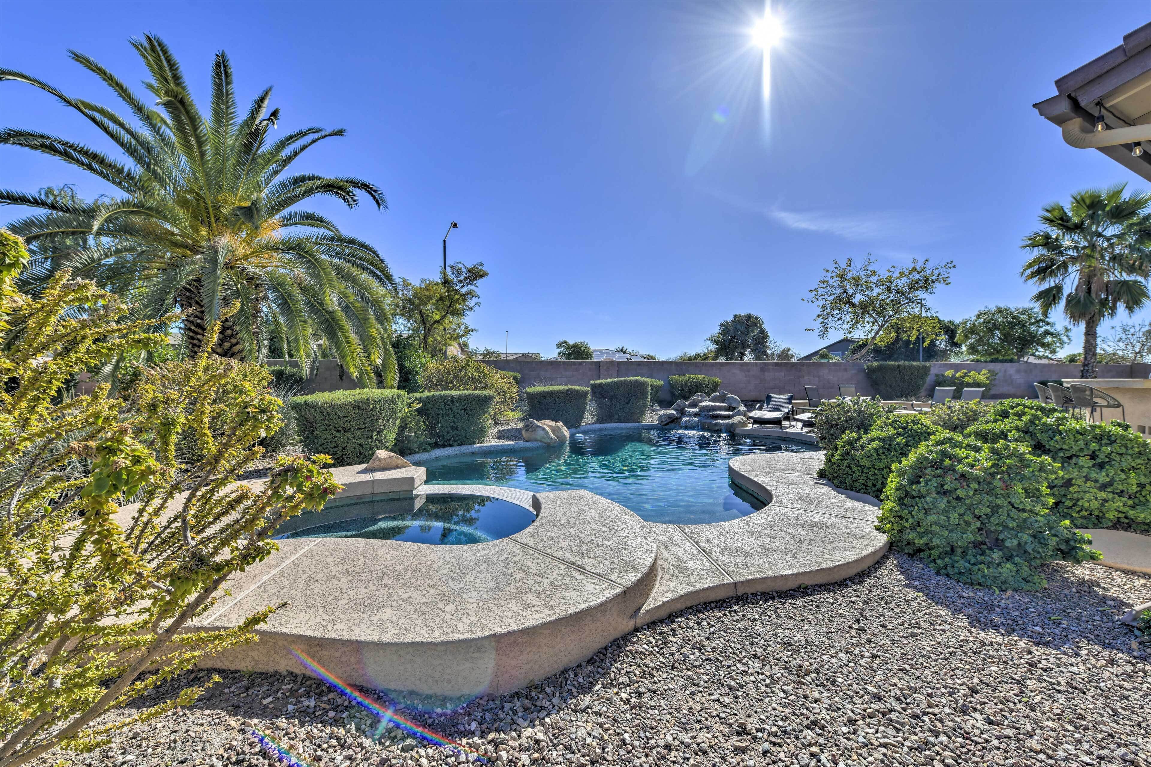 A swimming pool with a curved design, surrounded by gravel, palm trees, and well-maintained bushes.
