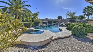 A swimming pool with a curved design, surrounded by gravel, palm trees, and well-maintained bushes.