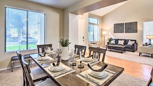 A dining area with a long table set for six, a living room with a sofa and a coffee table, and a hallway leading to another room.