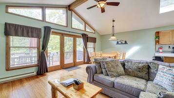 A spacious living room with a wooden floor, a sofa with patterned cushions, a wooden coffee table, and a ceiling fan.