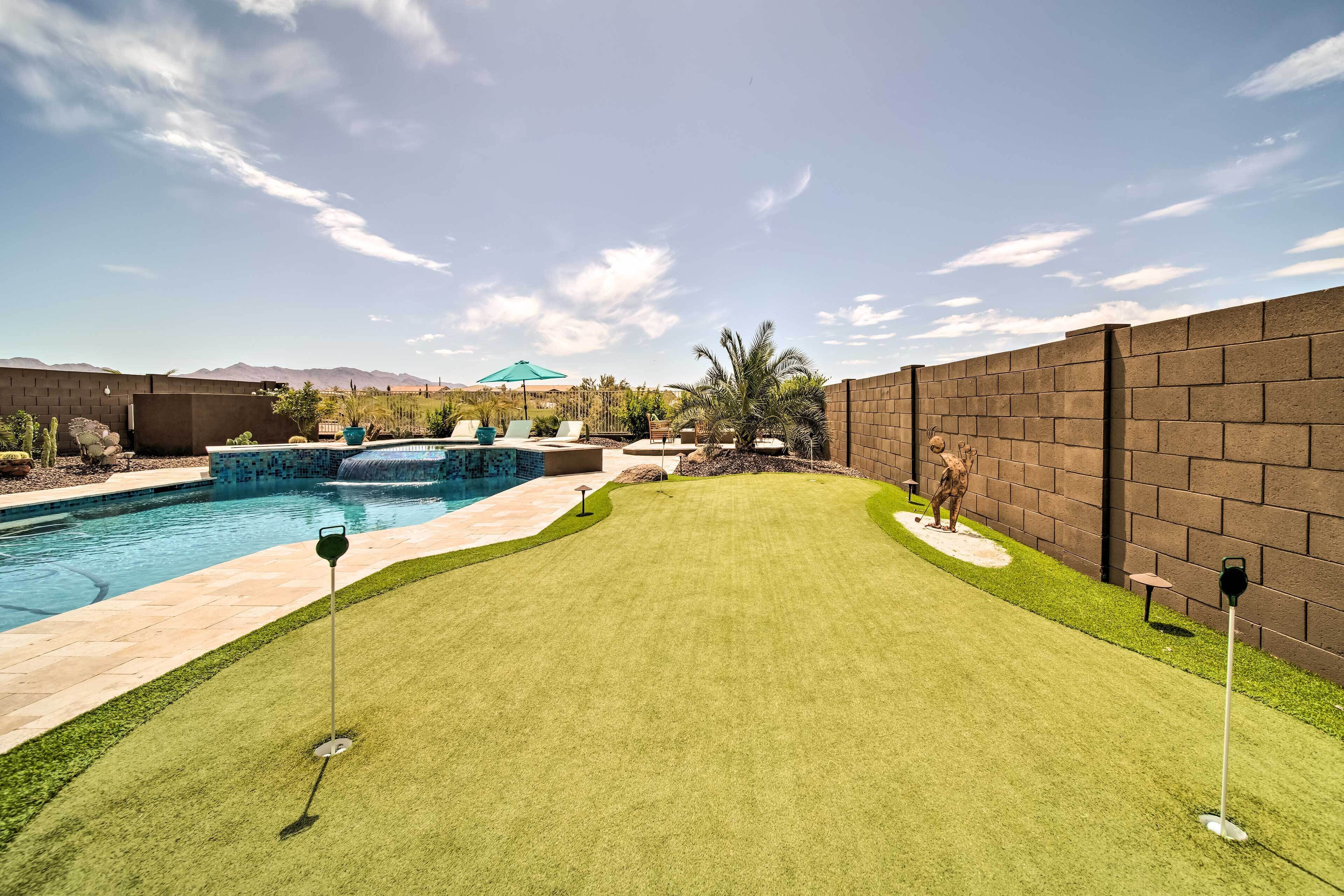 A backyard with a swimming pool, artificial grass, and a brick wall.