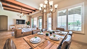 Un comedor con una mesa de madera dispuesta para cuatro personas, rodeada de sillas de cuero, y un candelabro colgando.