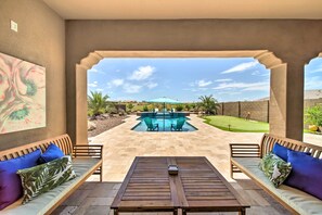 A patio area with a pool, wooden furniture, and a view of the pool and landscape. - Resort-style Pool & Spa: Upscale Goodyear Home (Goodyear)