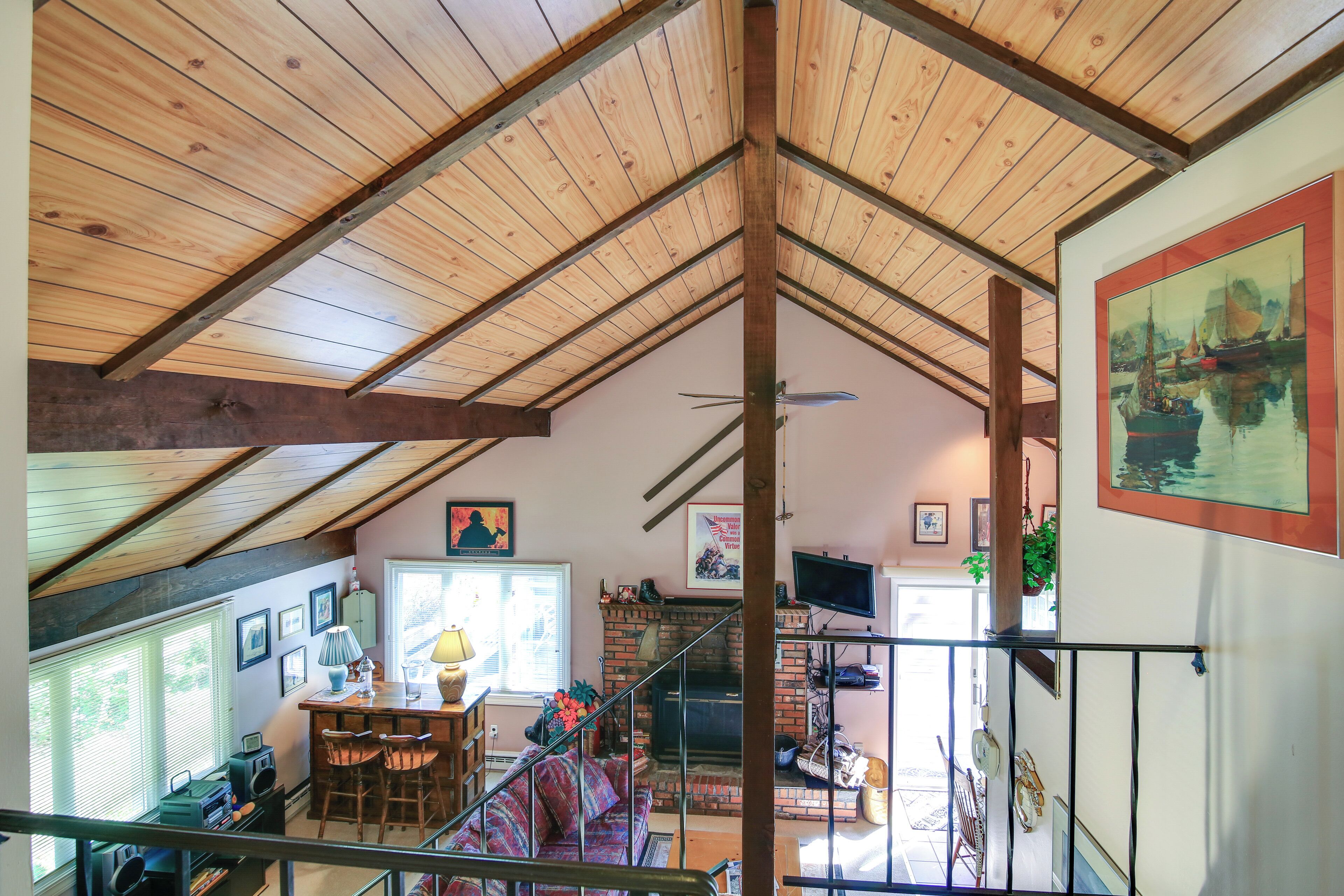 A spacious loft with a high ceiling, exposed wooden beams, a fireplace, a staircase, and a large window providing natural light.