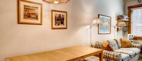 Una sala de estar acogedora con una mesa de madera, un sofá de cuadros y fotografías enmarcadas en la pared.
