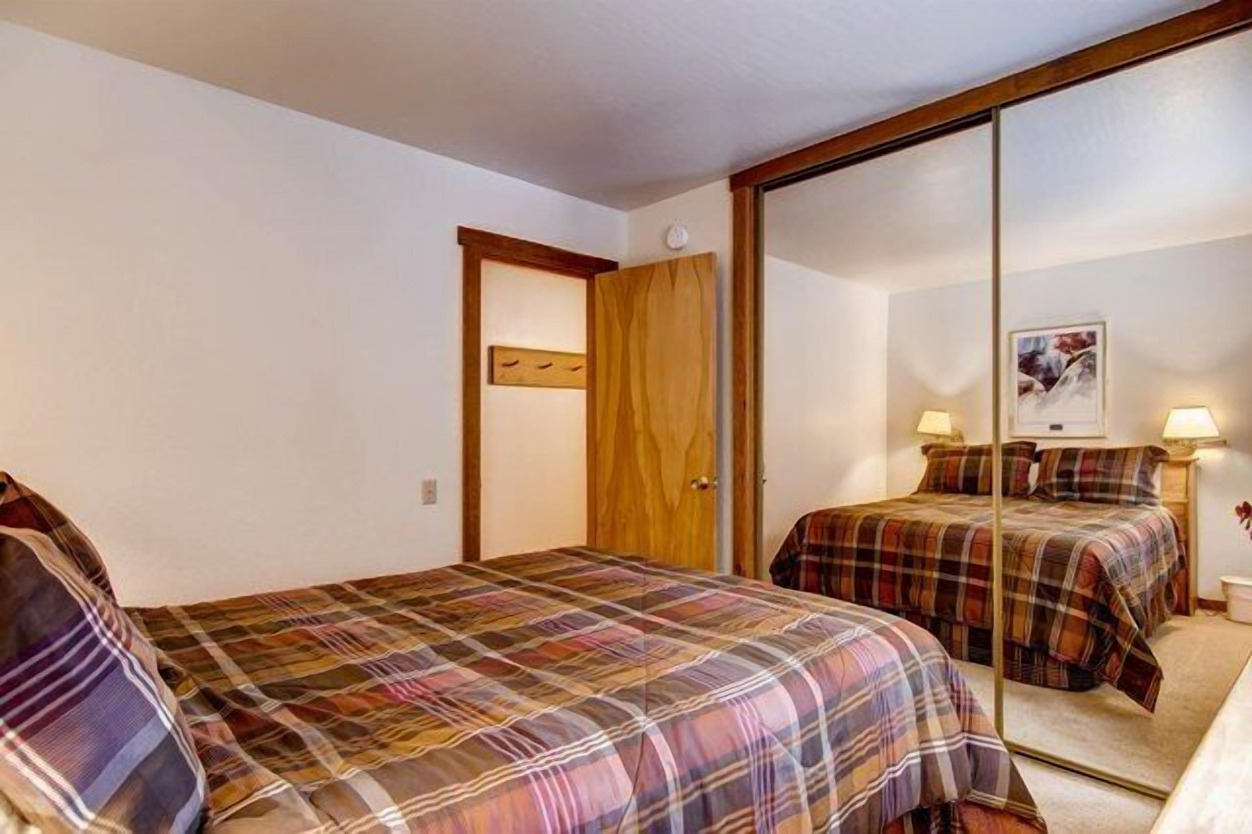Une chambre avec deux lits, une porte en bois et un miroir qui reflète les lits.