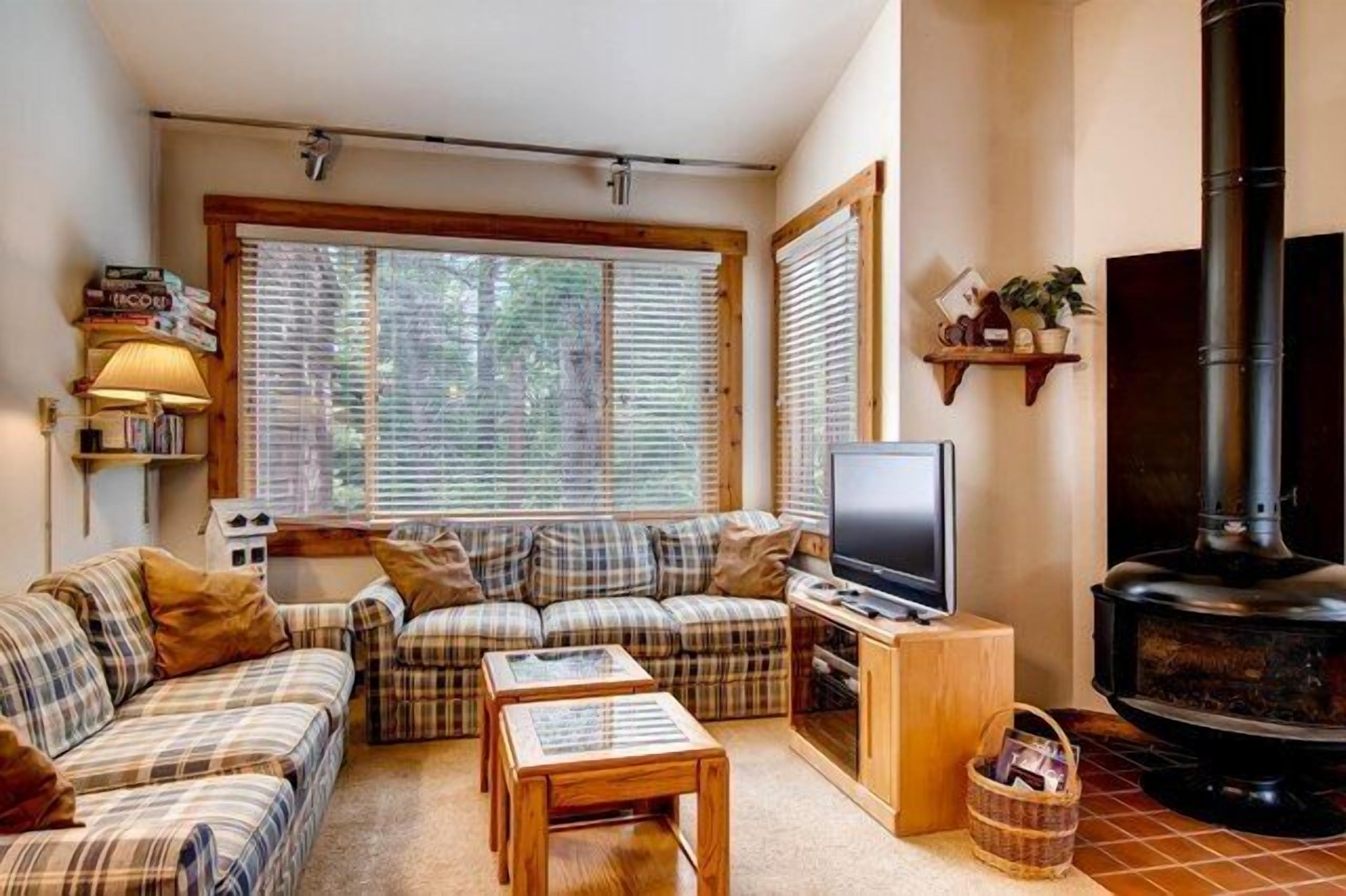 A cozy living room with a sofa set, a television, and a wood-burning stove.