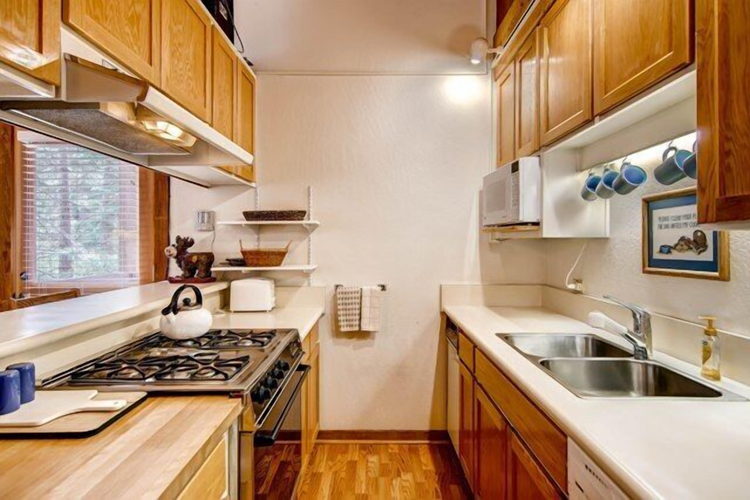A compact kitchen with wooden cabinets, a gas stove, a sink, and a window with blinds.