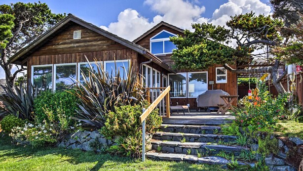 Une cabane en bois avec un escalier en pierre menant à une terrasse, le tout entouré d’une végétation luxuriante et d’arbres.