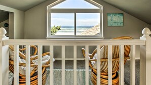 Un balcon avec des fauteuils en osier, une vue sur l’océan et une œuvre d’art encadrée accrochée au mur.