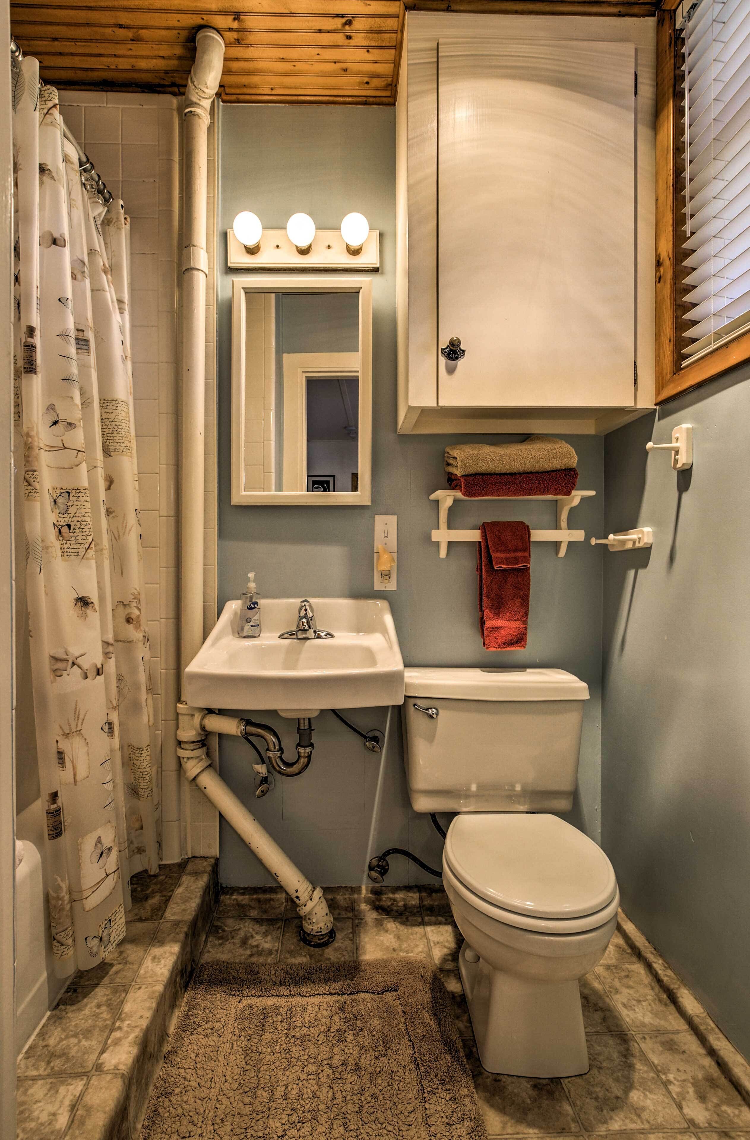 A small bathroom with a sink, mirror, and toilet. There is a shower curtain with a pattern, a towel rack, and a light fixture above the mirror.