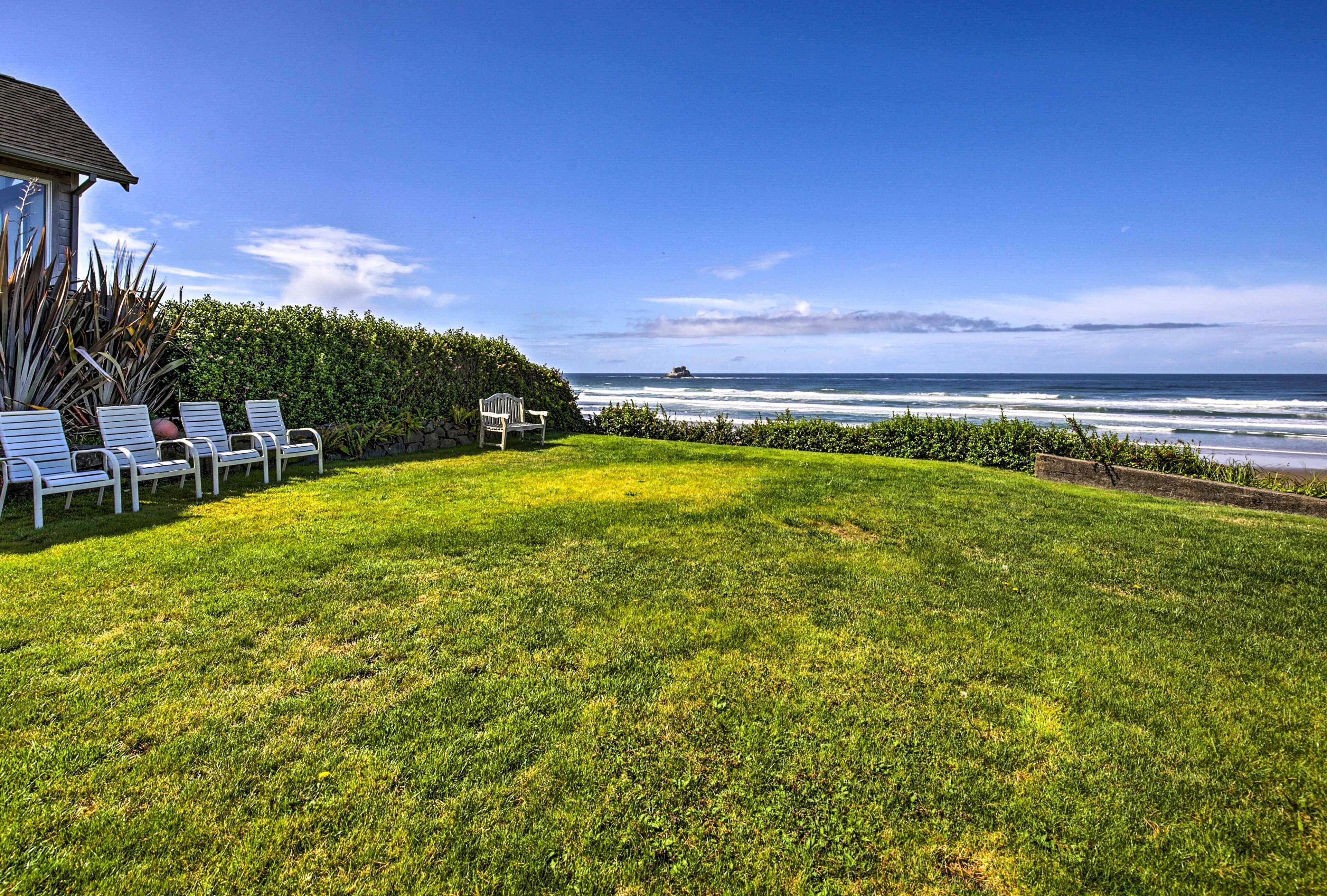 A grassy lawn with white lounge chairs and a view of the ocean.