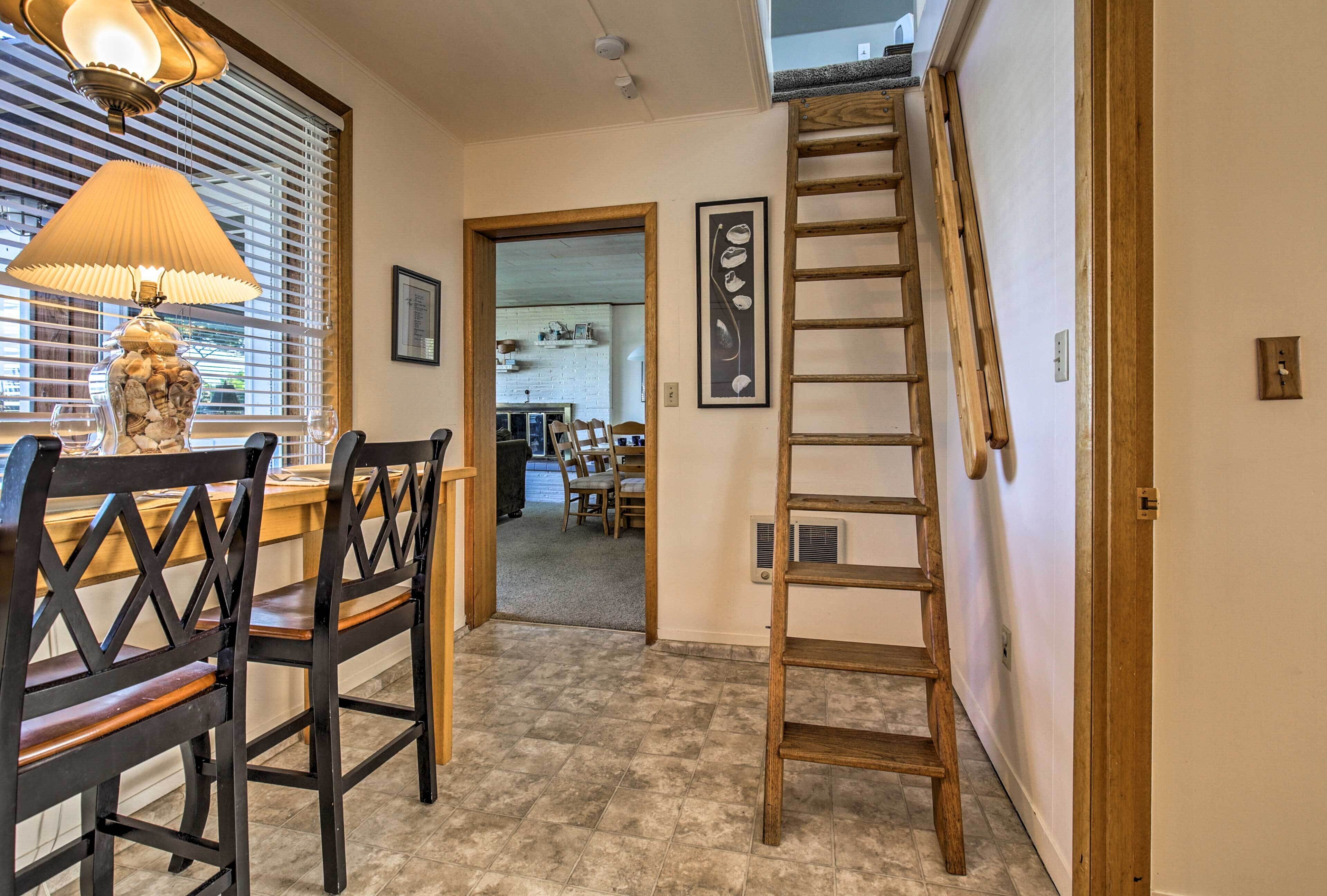 A dining area with wooden chairs and a table, a lamp, a ladder, and a door leading to another room.