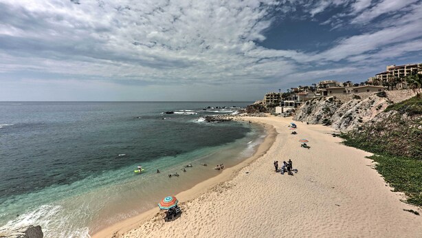 Une plage aux eaux cristallines, un rivage sablonneux et des bâtiments situés sur une falaise.