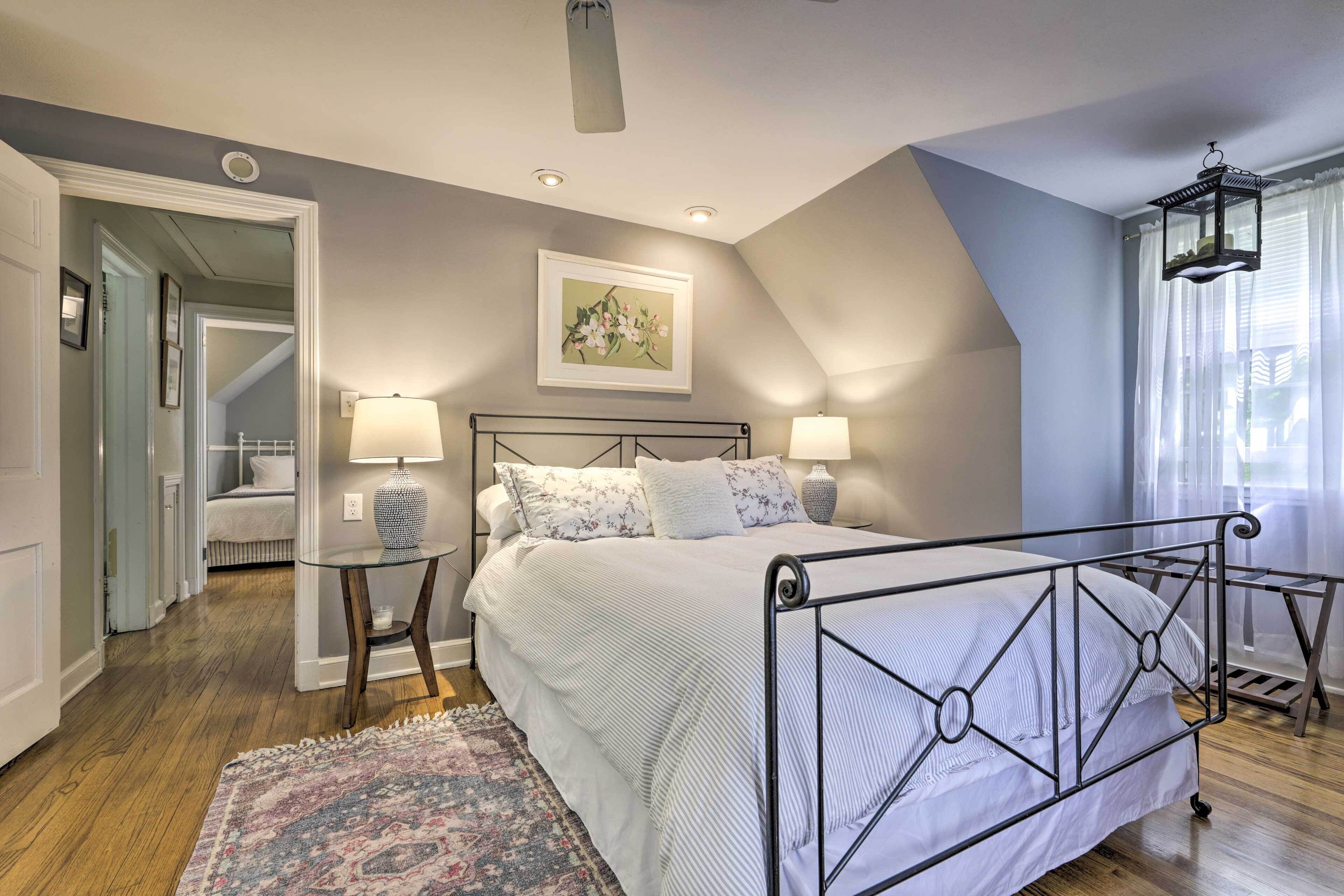 Une chambre à coucher comprenant un lit, deux tables de chevet, une commode, un tapis et une fenêtre avec des rideaux.